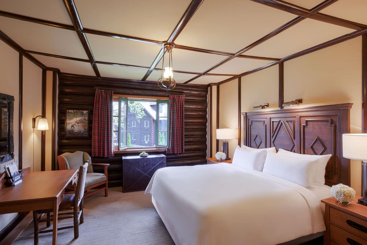 Een hotelkamer met een groot bed, een bureau, een stoel, een nachtkastje, een lamp en een raam met gordijnen.