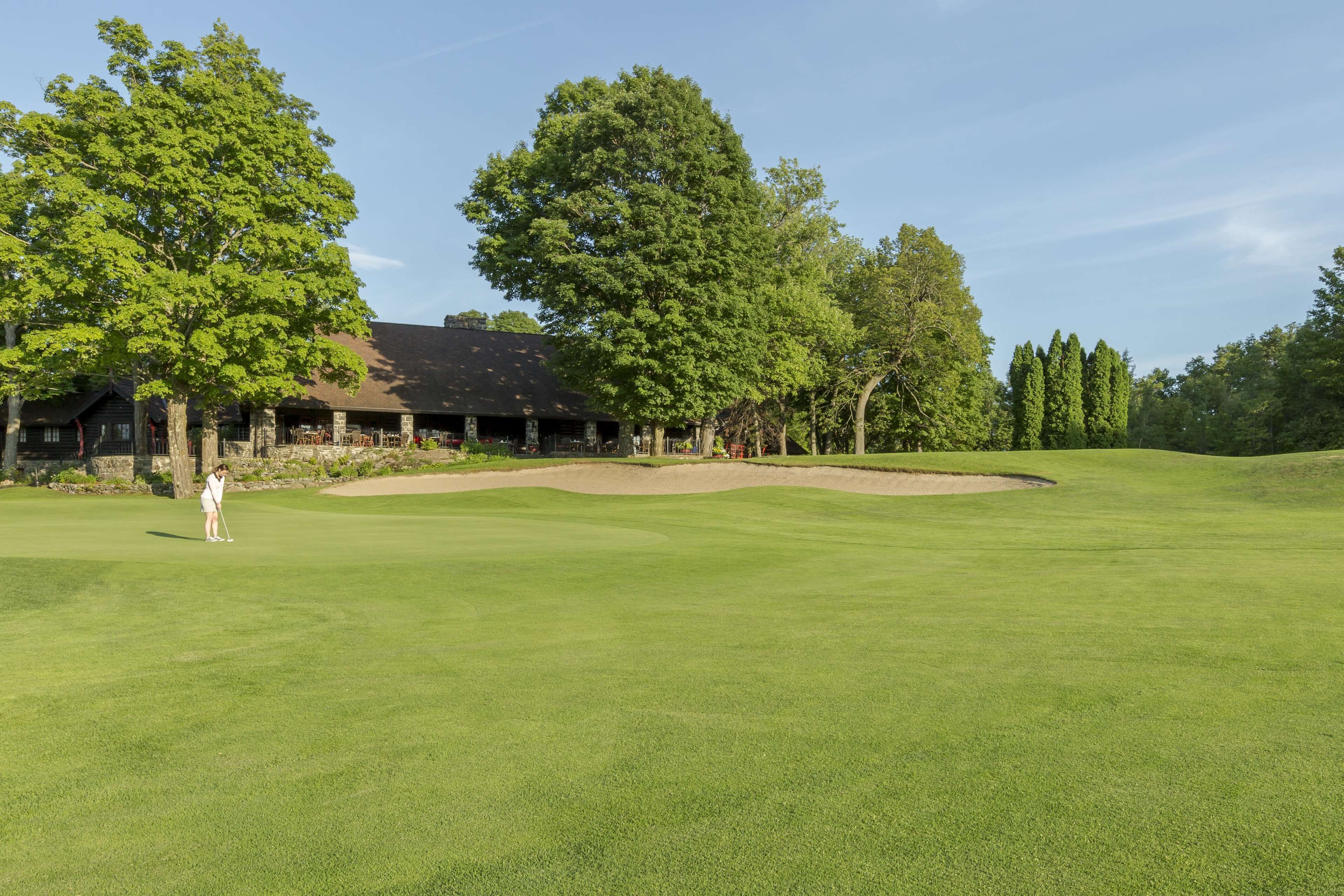 A golf course with a clubhouse, trees, and a clear sky.