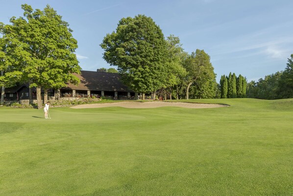 Un parcours de golf doté d’un club-house, d’arbres et offrant une vue sur un ciel dégagé.