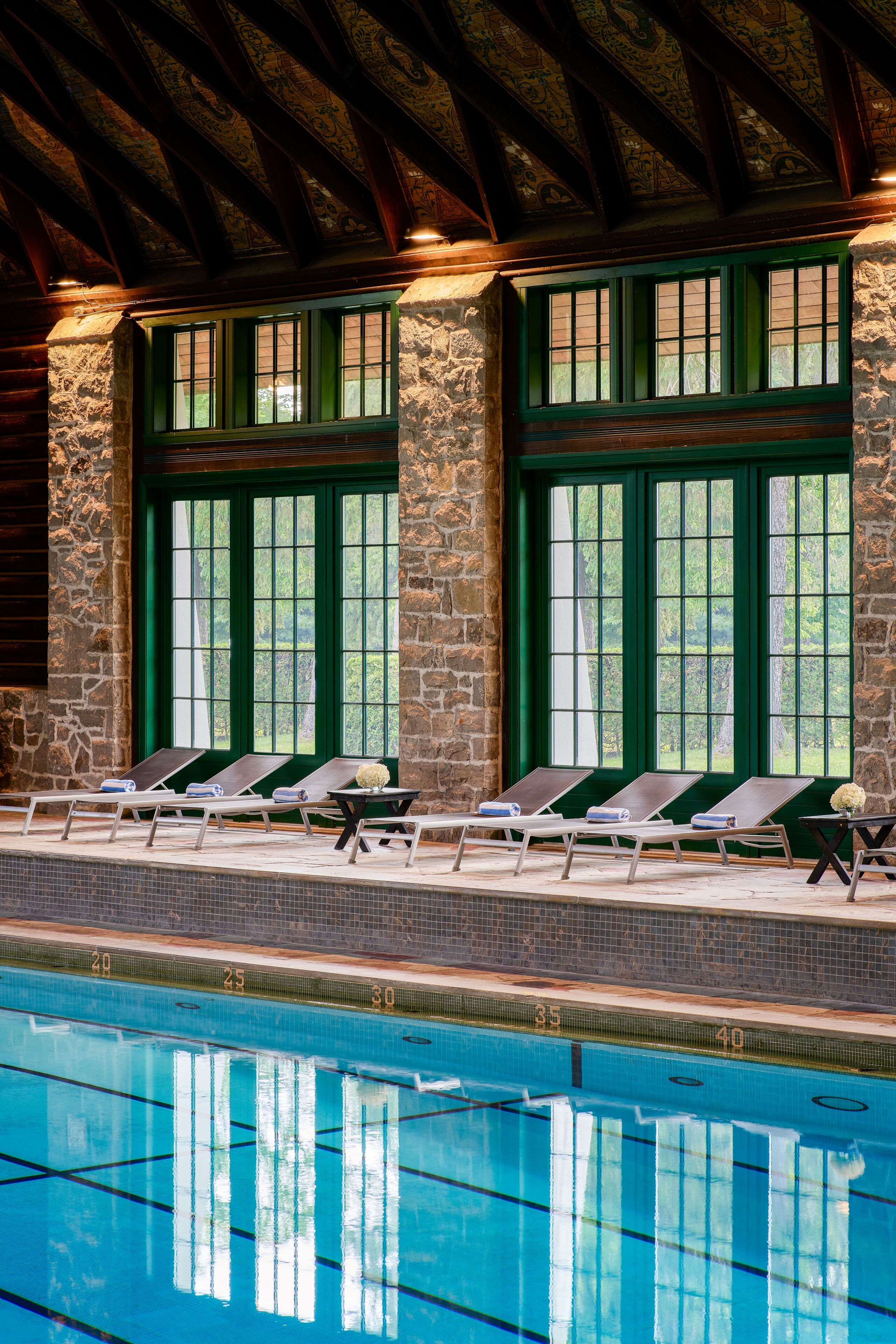 Zona de piscina con sillas de descanso, paredes de piedra y ventanas amplias.