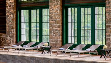 Zona de piscina con sillas de descanso, paredes de piedra y ventanas amplias.