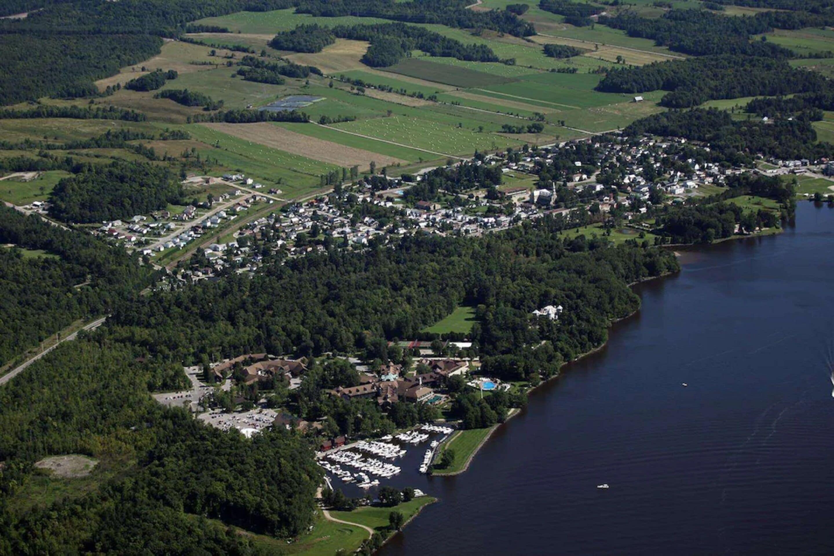 An aerial view of a lakeside town with residential areas, a marina, and surrounding greenery.