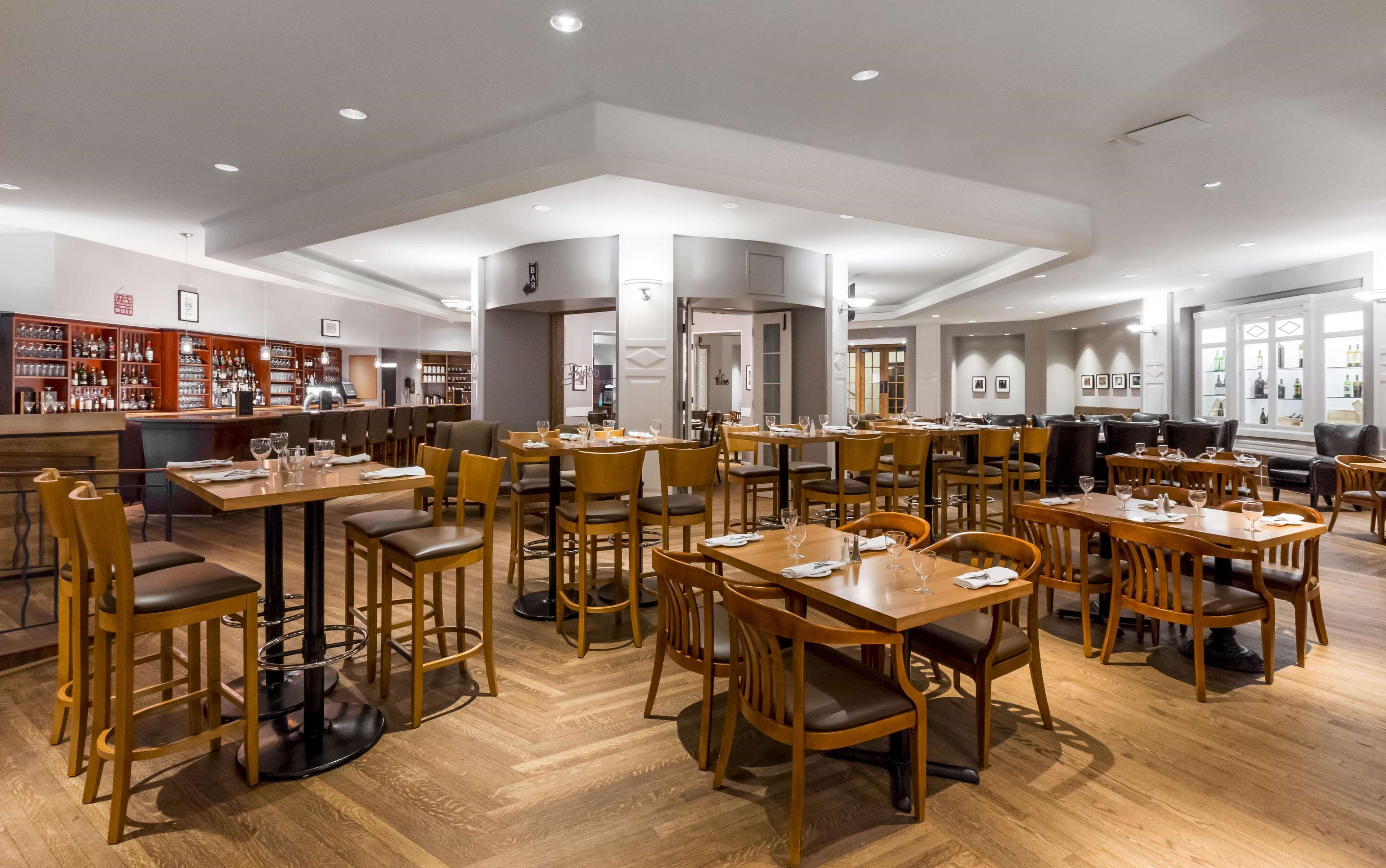 A spacious restaurant with multiple dining tables and chairs, a bar area with shelves of bottles, and a modern interior design.