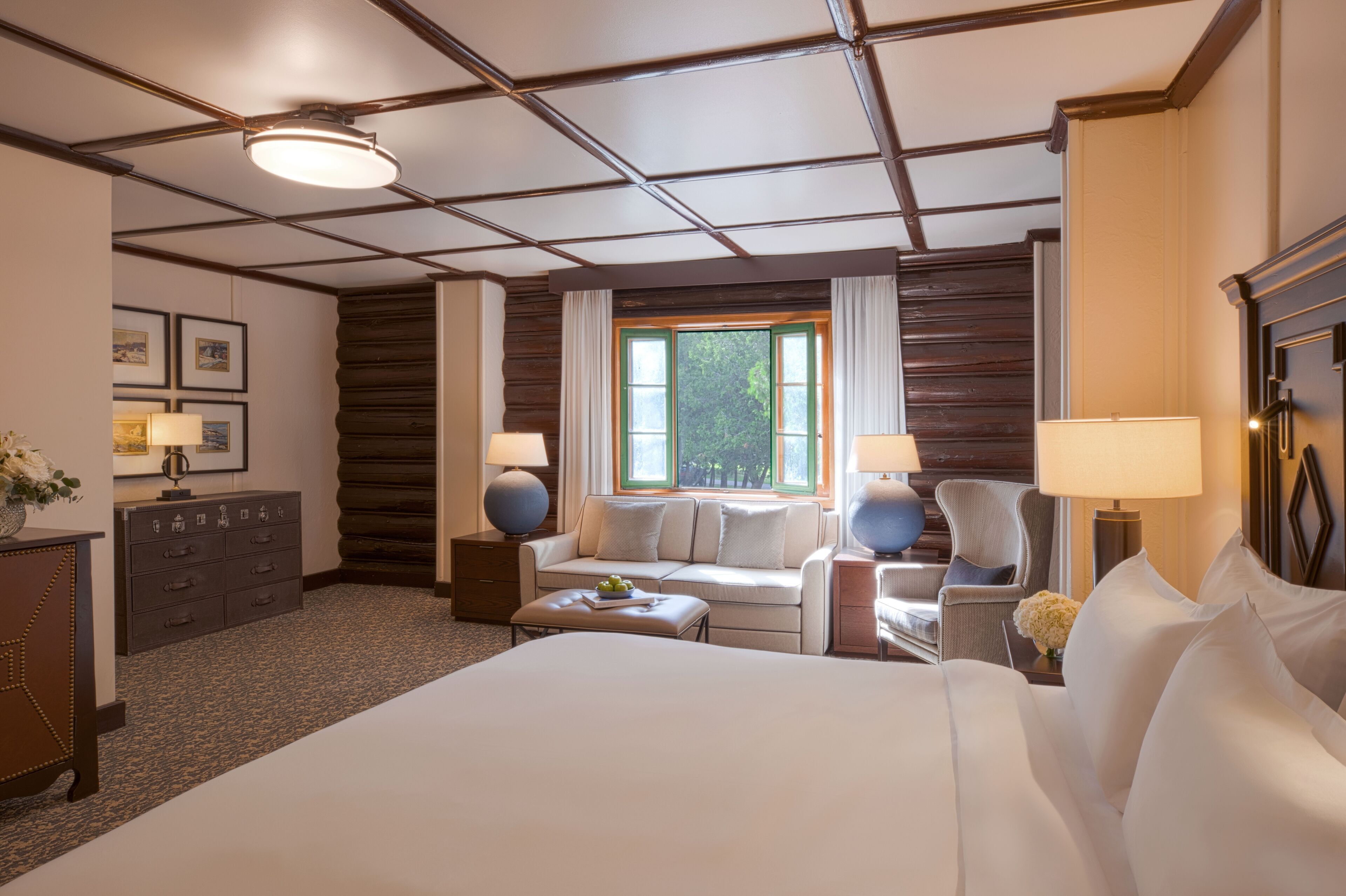 A hotel room with a large bed, a sofa, a chair, a desk, and a window with curtains.