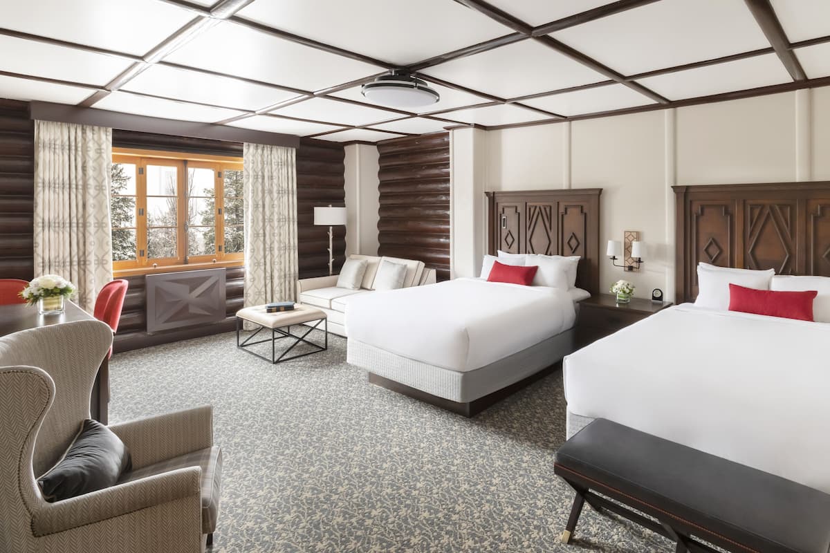 Een hotelkamer met twee bedden, een bank, een stoel, een bureau en een raam met gordijnen.