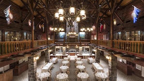 Un comedor amplio con techos altos de madera y candelabros, con varias mesas dispuestas para los comensales.