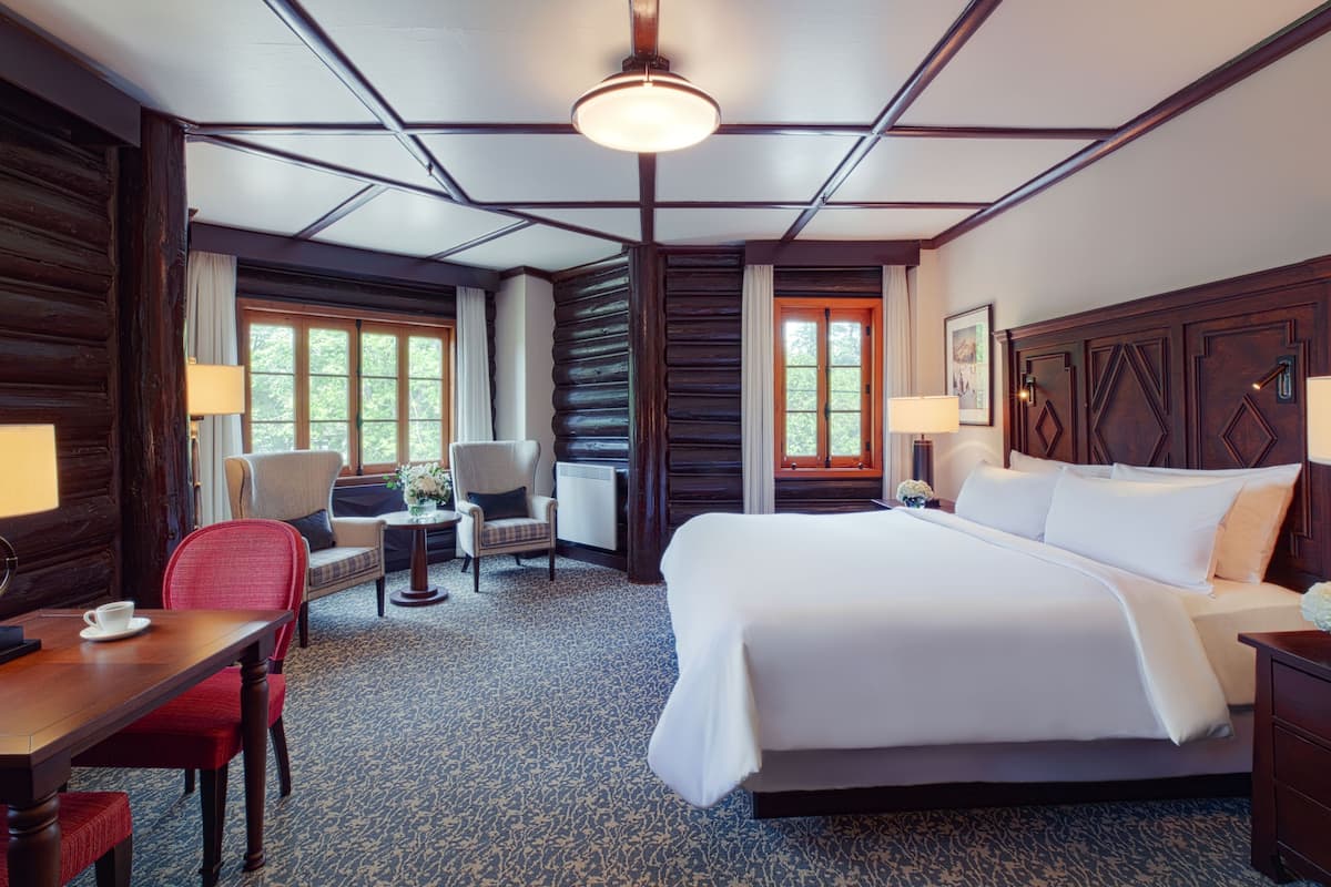 Een hotelkamer met een groot bed, een bureau met stoel, een kleine tafel met stoel, en een raam.