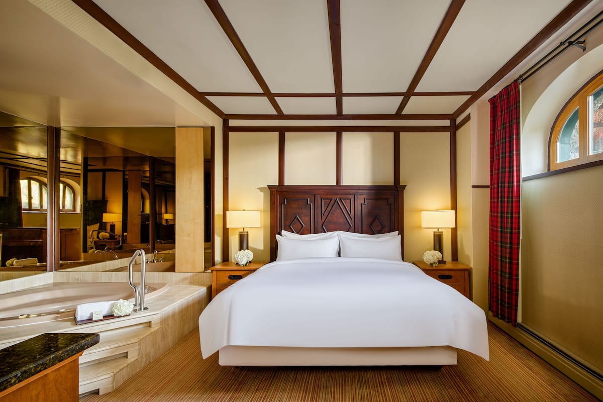 Een hotelkamer met een groot bed, een badkamer met bad, een spiegel en een raam met gordijnen.