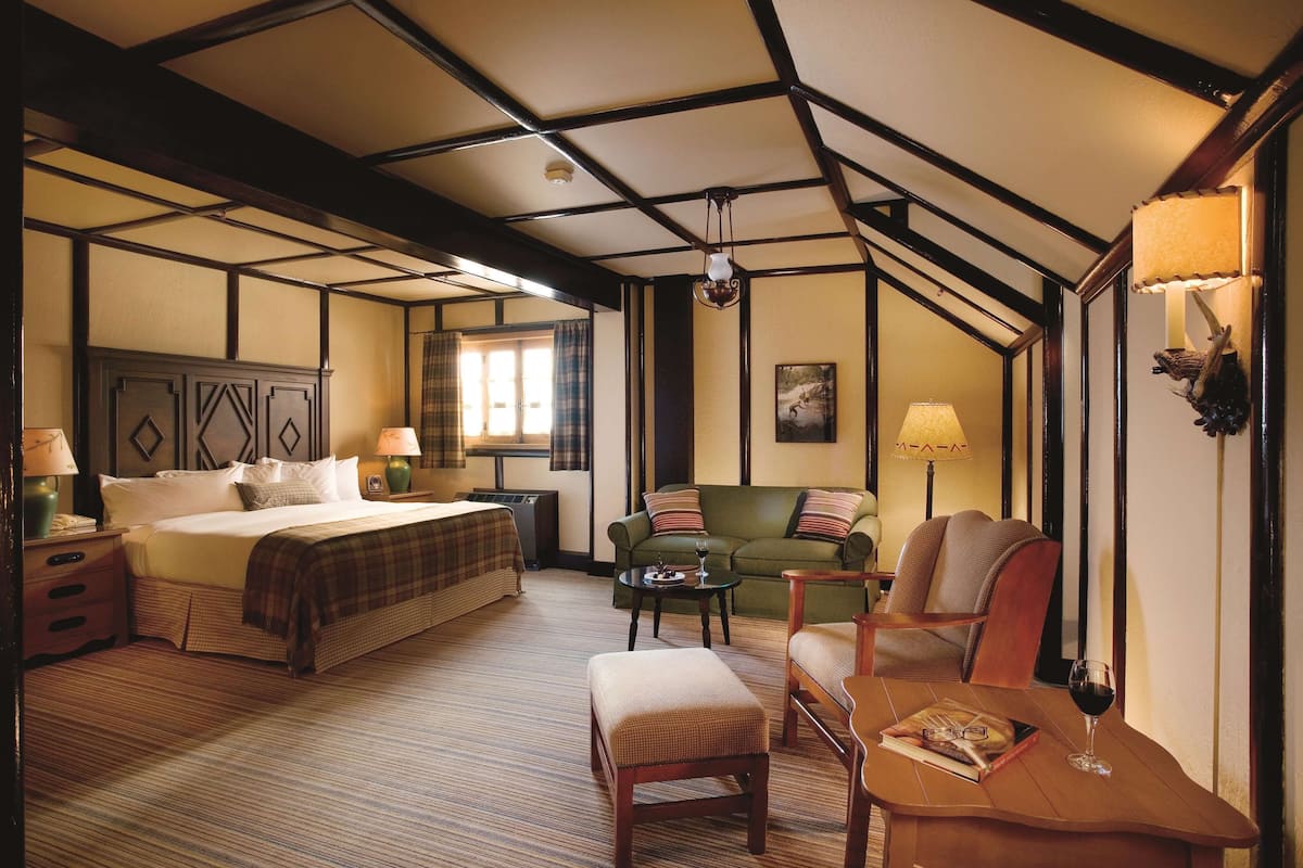 Een hotelkamer met een groot bed, een groene bank, een houten tafel met een glas wijn, en een lamp.