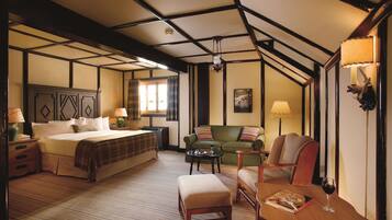 Una habitación de hotel con una cama grande, un sofá verde, una mesa de madera con una copa de vino y una lámpara.