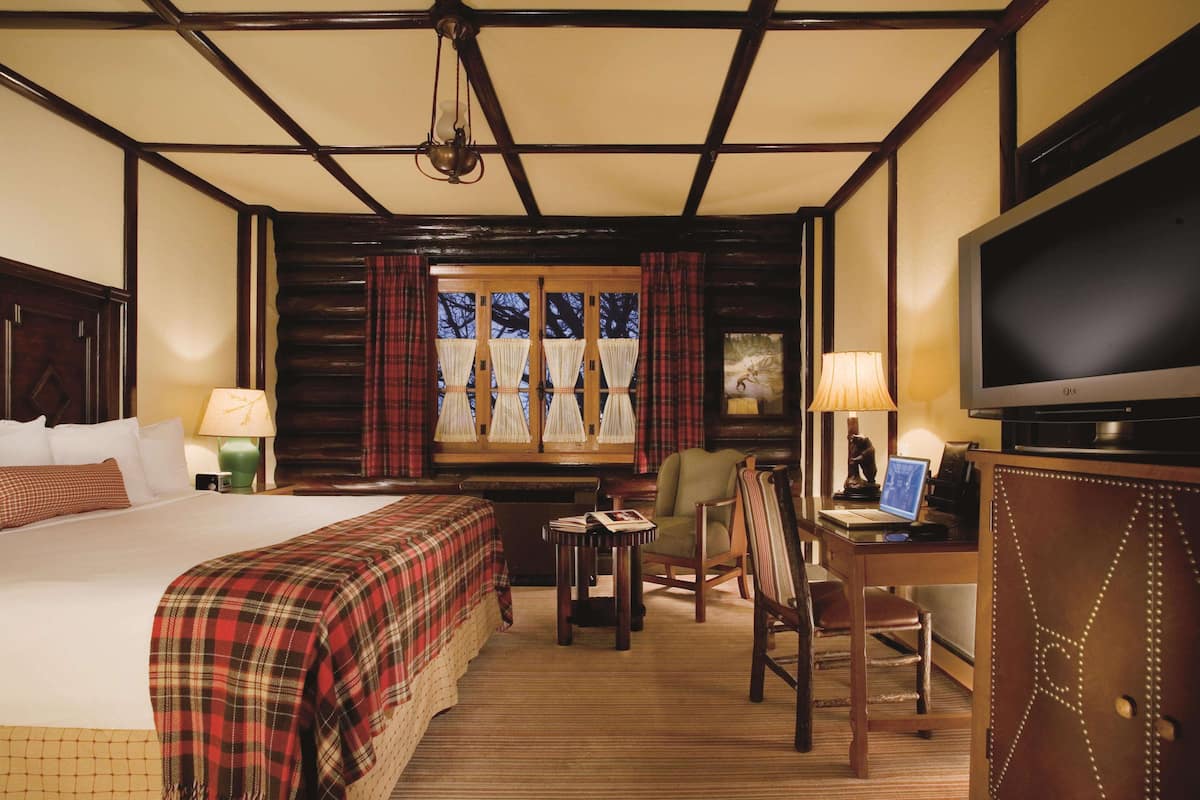 Een hotelkamer met een bed, een bureau met een computer, een televisie en een raam met gordijnen.