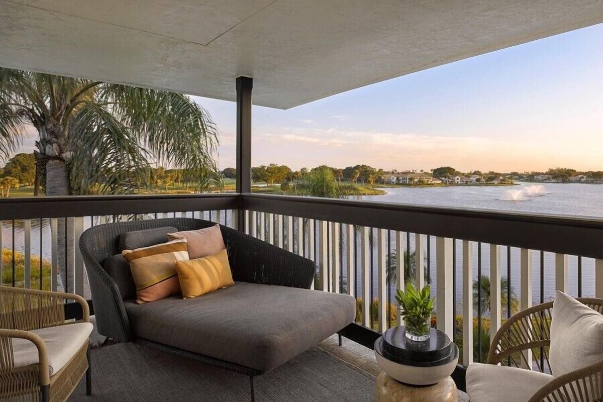 Een balkon met een bank en stoelen, met uitzicht op een meer en huizen en bomen.