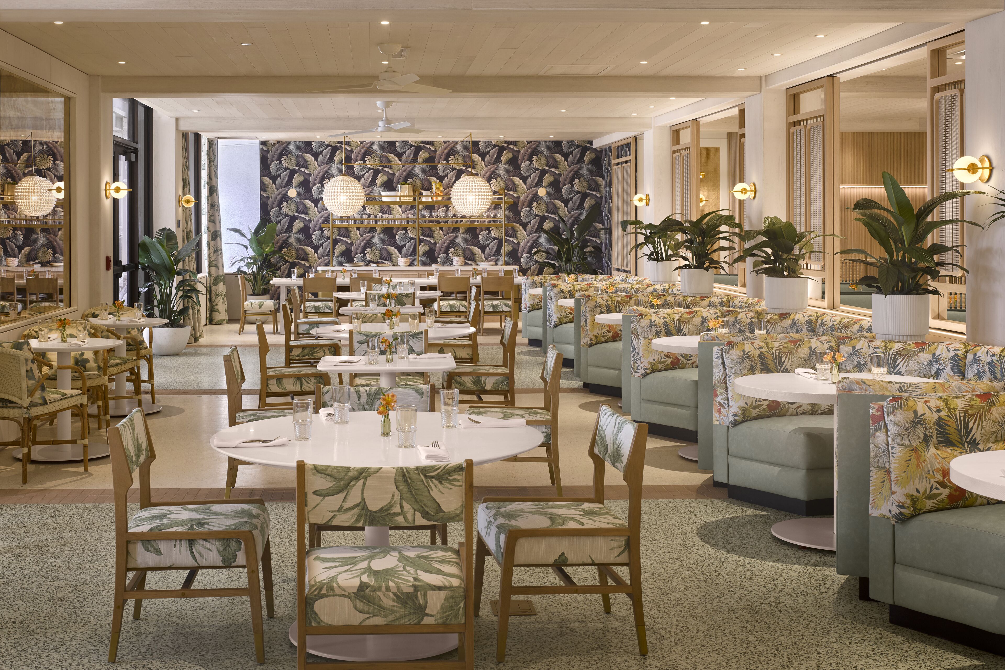 Ein geräumiges Restaurant mit runden Tischen und Stühlen, einer gemusterten Wand und Zimmerpflanzen.