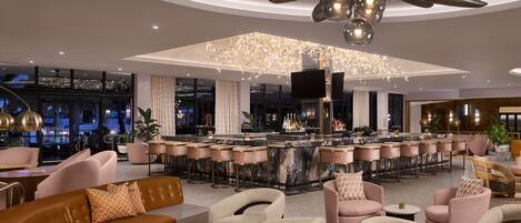 A modern bar area with a marble countertop, multiple bar stools, and a large chandelier.