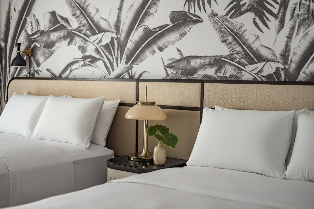 Een hotelkamer met een bed, nachtkastje, lamp en een muur met een tropisch bladmotief.