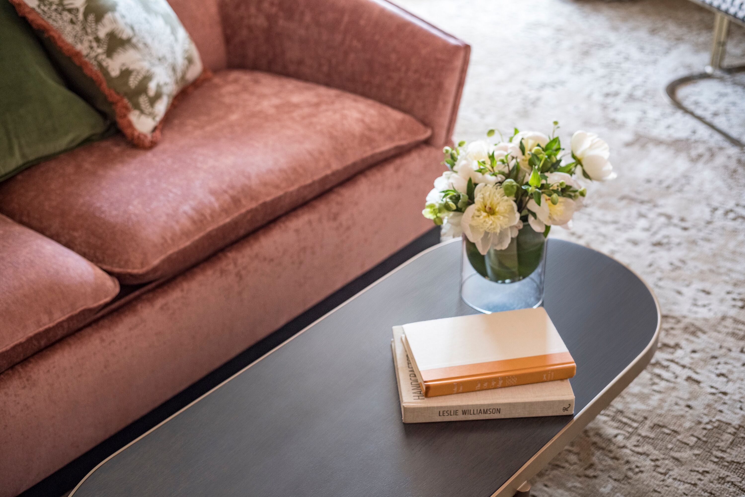 Een moderne woonkamer met een bruine bank, een zwarte salontafel en een vaas met witte bloemen.