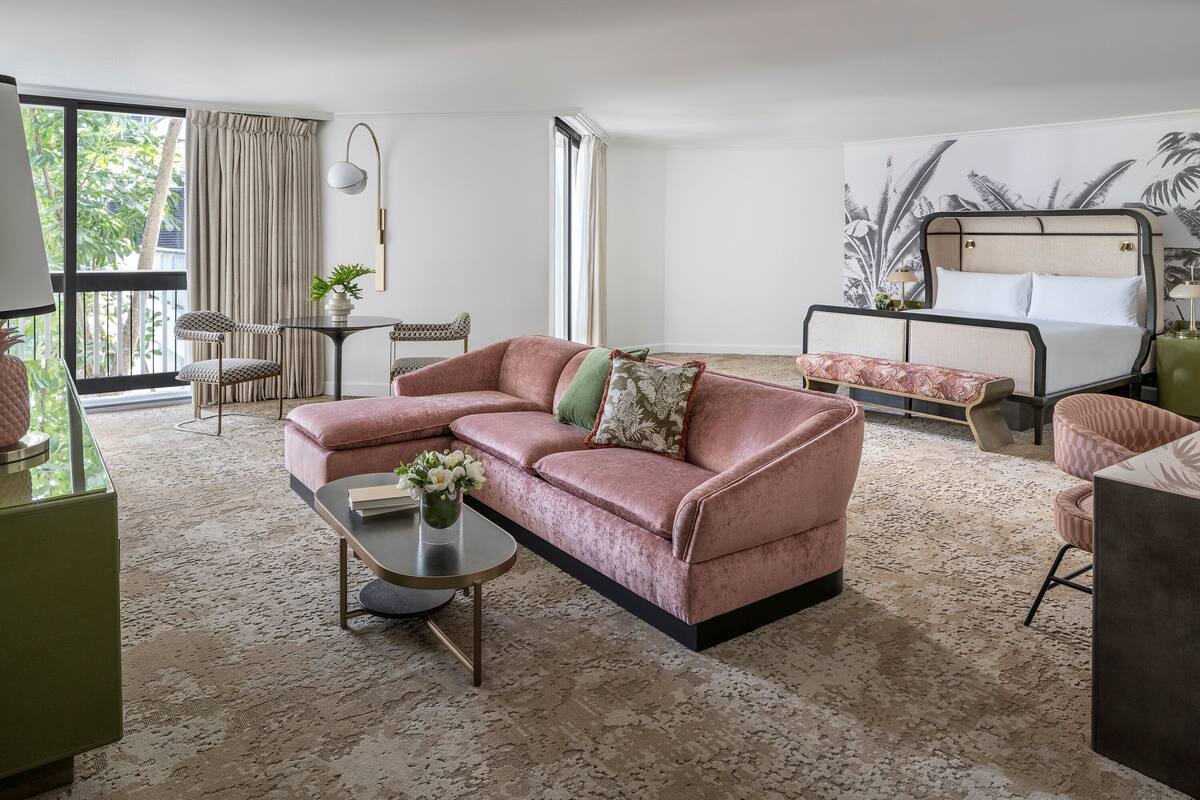 Een moderne woonkamer met een roze modulaire bank, een ronde salontafel en een groot raam met gordijnen.