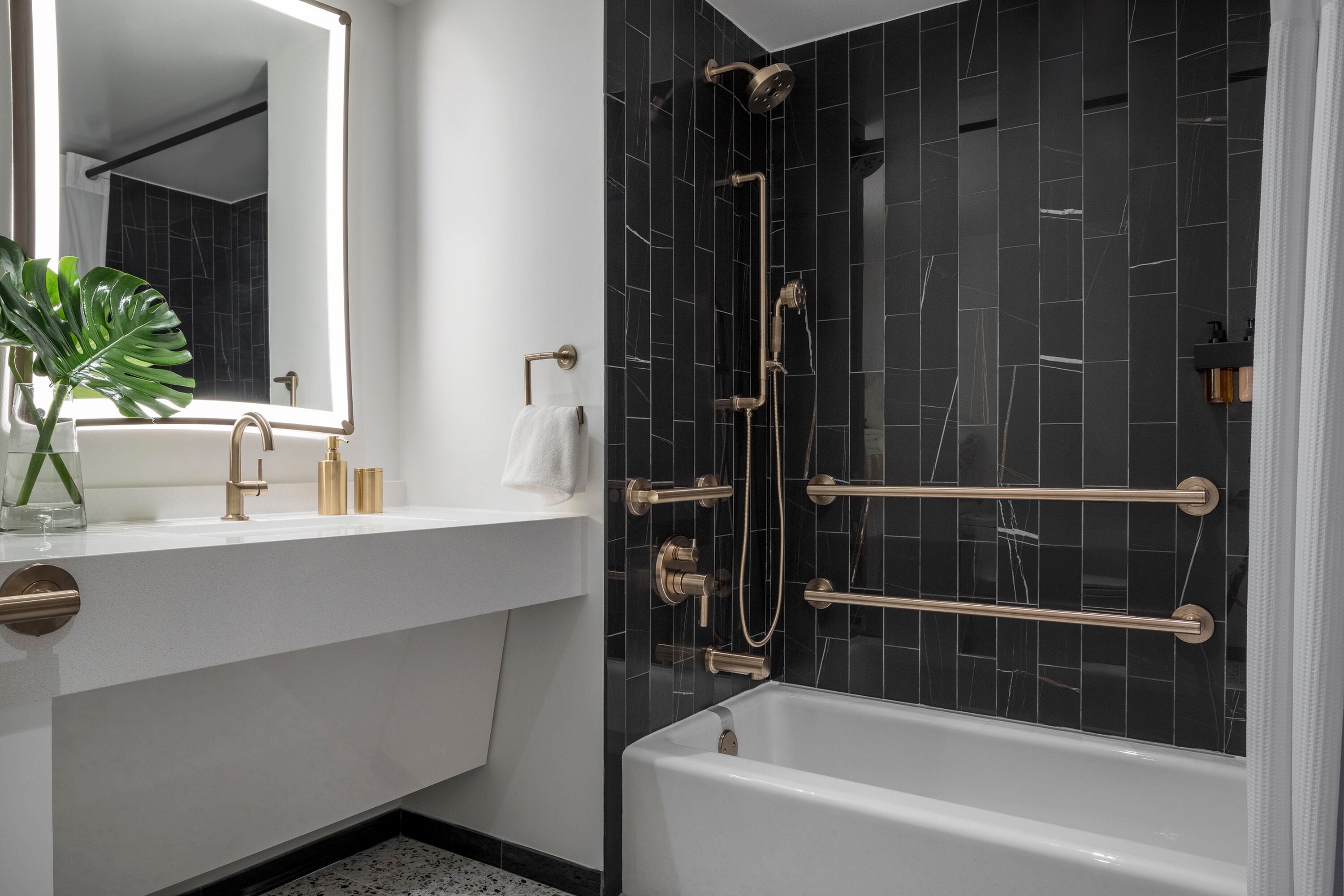 Ein modernes Badezimmer mit einem weißen Waschbecken, goldenen Armaturen, einem großen Spiegel und einer Dusche in schwarzer Fliesenoptik.
