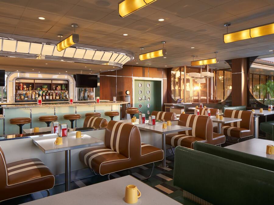 A retro-themed restaurant with booths and tables, a bar area, and a green wall with circular decorations.