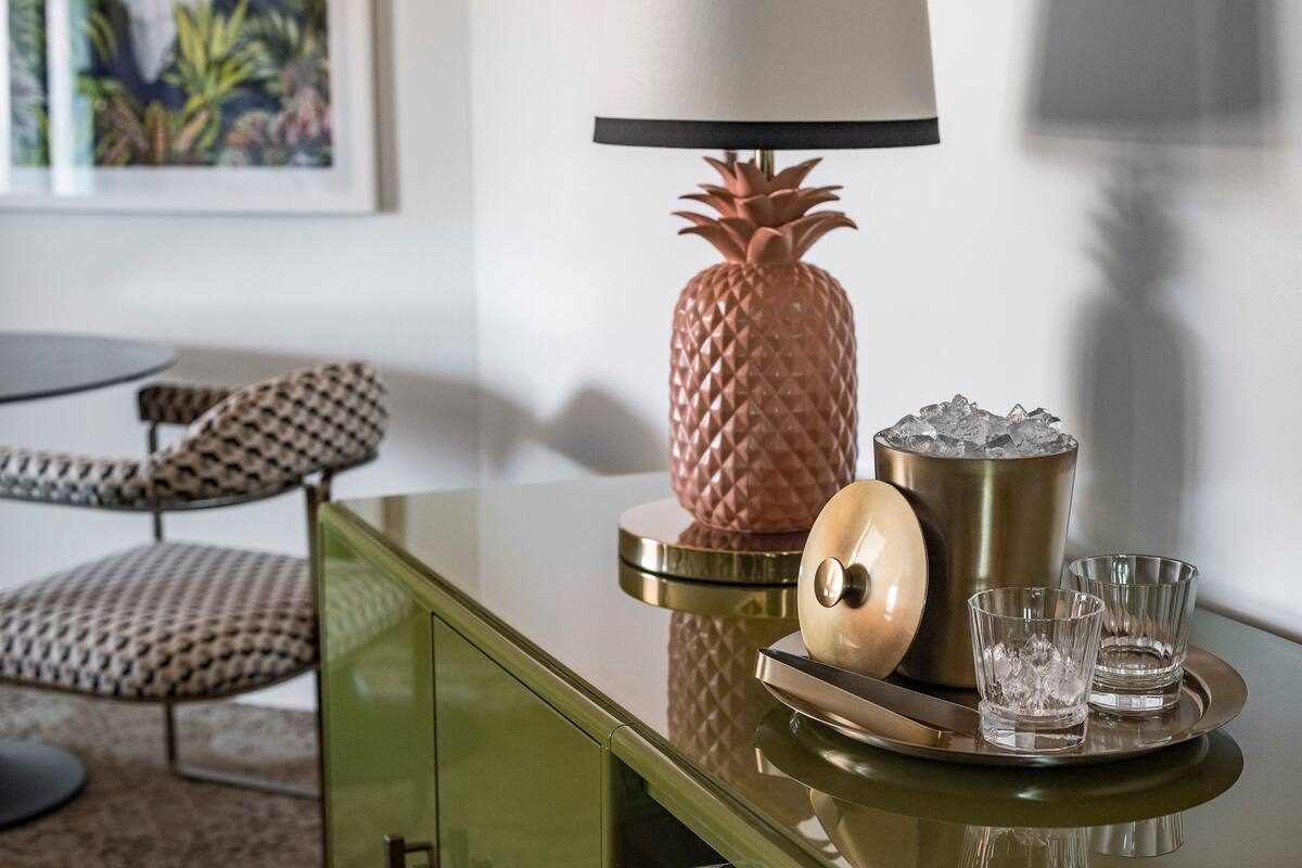 Een groen kastje met een lamp in de vorm van een ananas, een metalen bak en twee glaasjes op een dienblad.