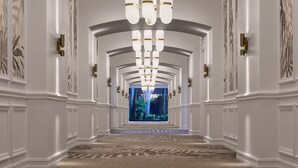 A grand hallway with a modern chandelier, white walls, and a carpeted floor. - PGA National Resort  (Palm Beach Gardens)