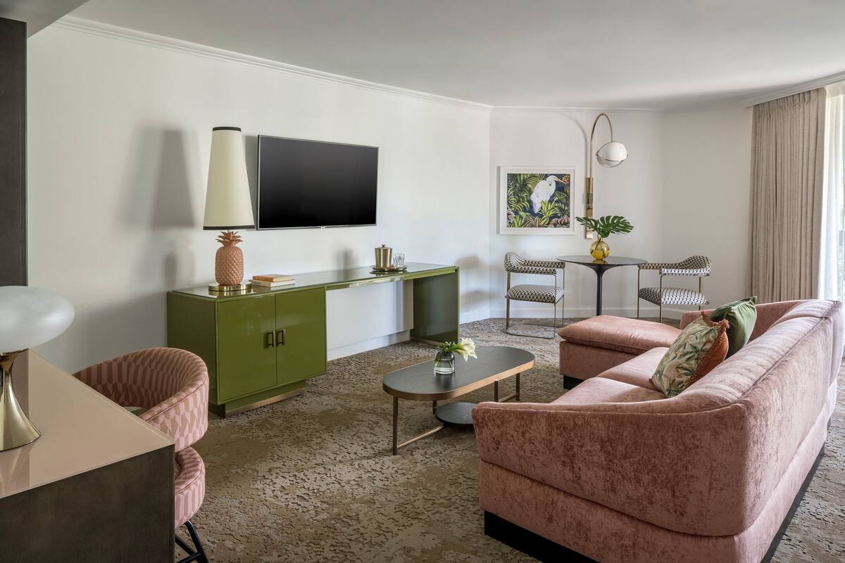 Een woonkamer met een groen kastje, een roze bank, een salontafel en een televisie aan de muur.