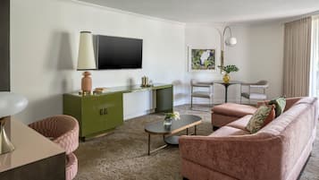 Una sala de estar con un mueble verde, un sofá rosa, una mesa de centro y un televisor en la pared.