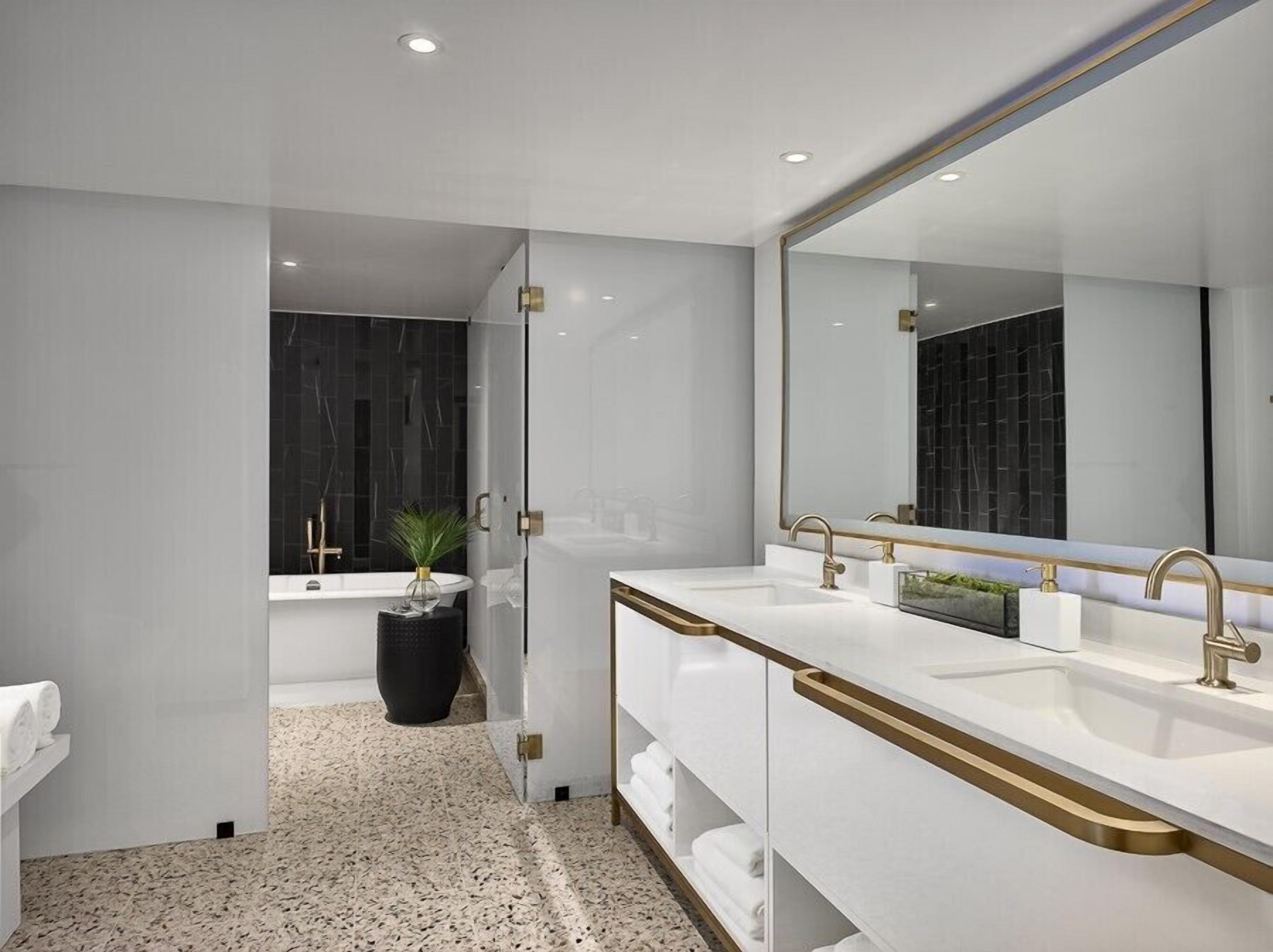 A modern bathroom with two sinks, a large mirror, and a bathtub.