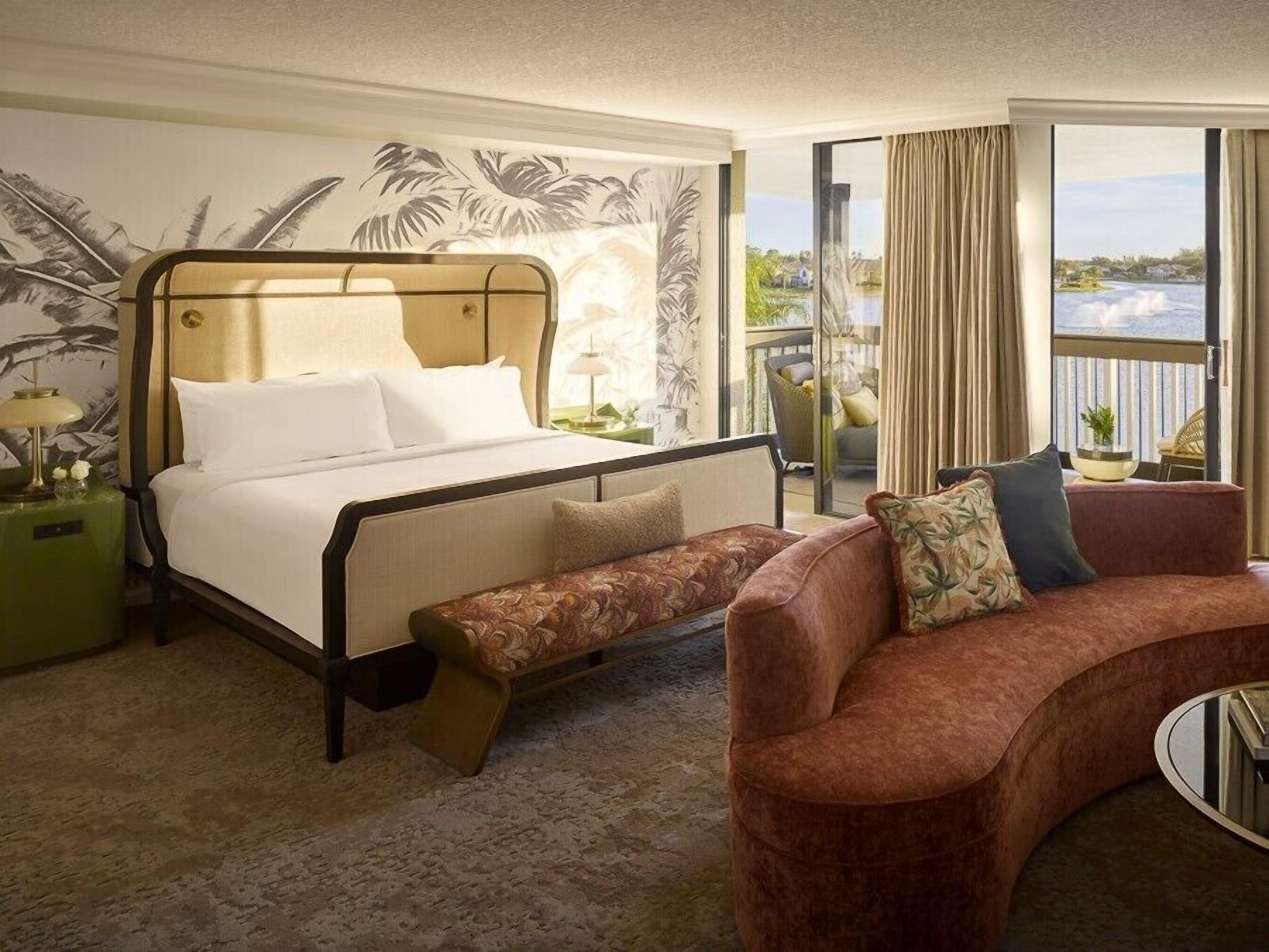 A hotel room with a bed, a bench, a sofa, and a view of the outdoors.