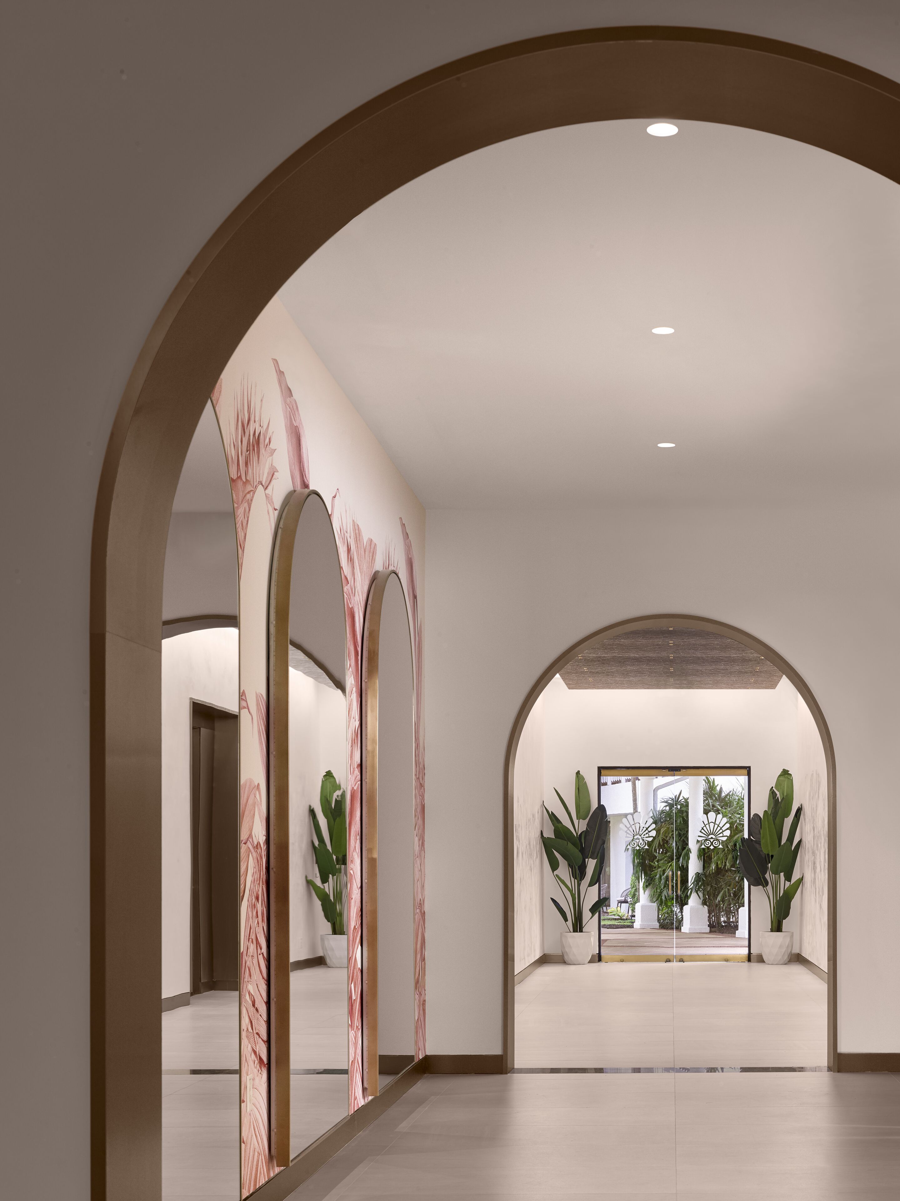 Un couloir moderne avec des portes en arc de cercle, des œuvres d’art murales en marbre et des plantes en pot.