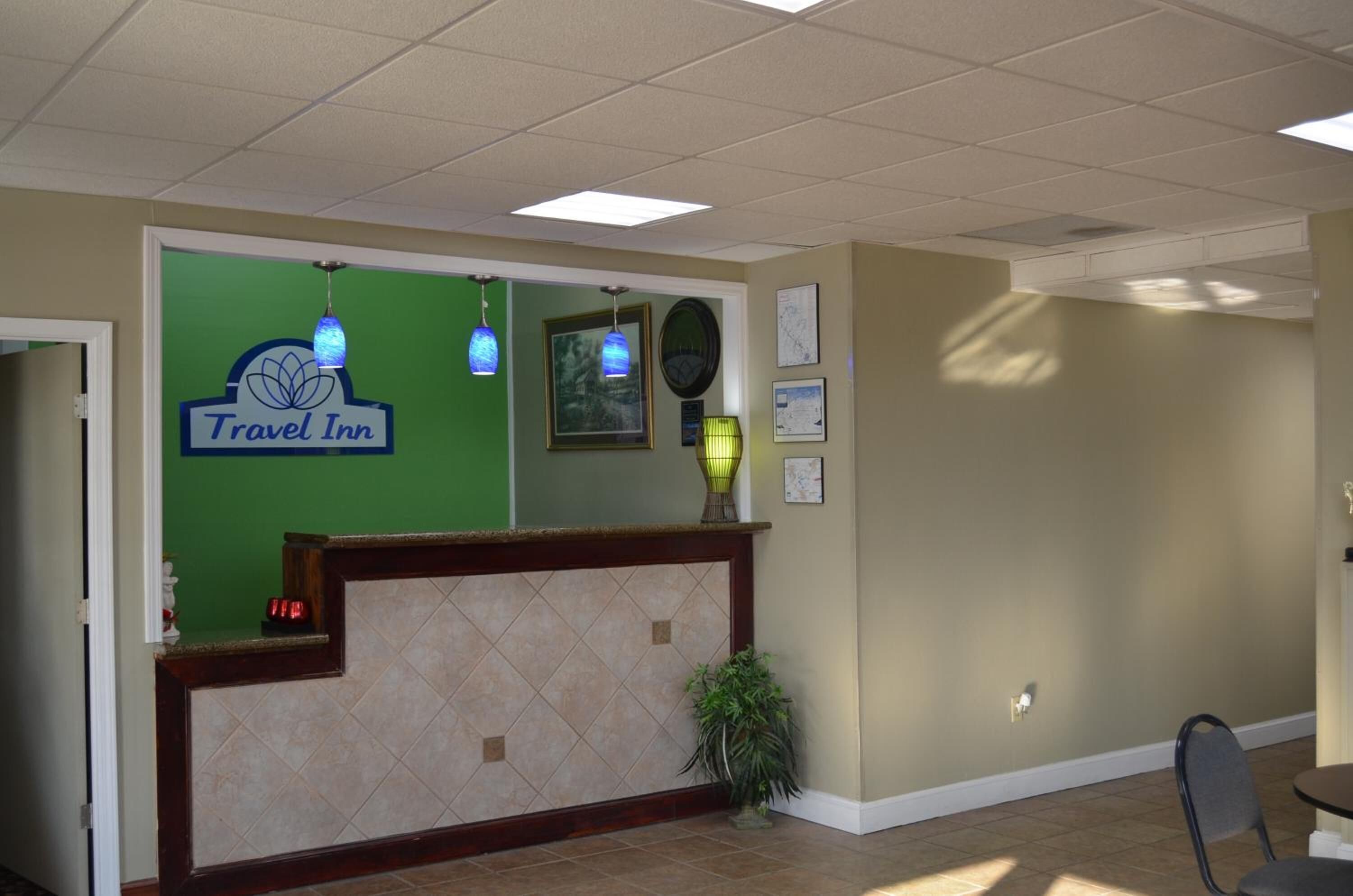 Un espace d’accueil avec un mur végétal, une enseigne « Travel Inn », un comptoir d’accueil, une plante et une carte affichée au mur.