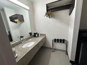 A bathroom with a granite countertop, a sink, a mirror, a towel rack, and a shelf with toiletries. - Travel Inn Kingsport (Kingsport)