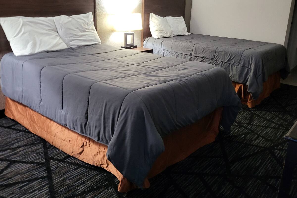 A hotel room with two beds, a nightstand, and a lamp.