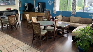 A room with a dining table, chairs, a sofa, a coffee machine, and a TV mounted on the wall.