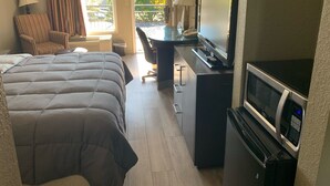A hotel room with a bed, a desk with a computer, a TV, and a microwave.