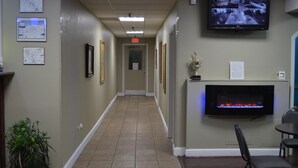 A hotel corridor with framed pictures on the walls, a television mounted on the wall, and a fireplace with a fire.