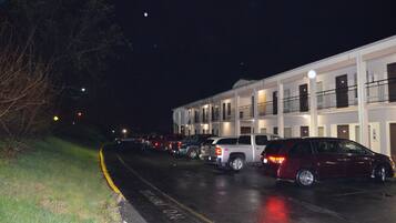 Una fila de coches aparcados frente a un motel con varios balcones y un exterior bien iluminado.