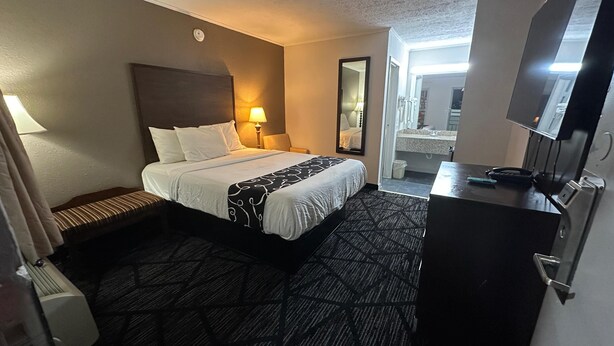 A hotel room with a bed, bedside lamp, dresser, and a mirror.