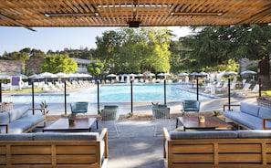 A poolside area with lounge chairs, umbrellas, and a wooden pergola.