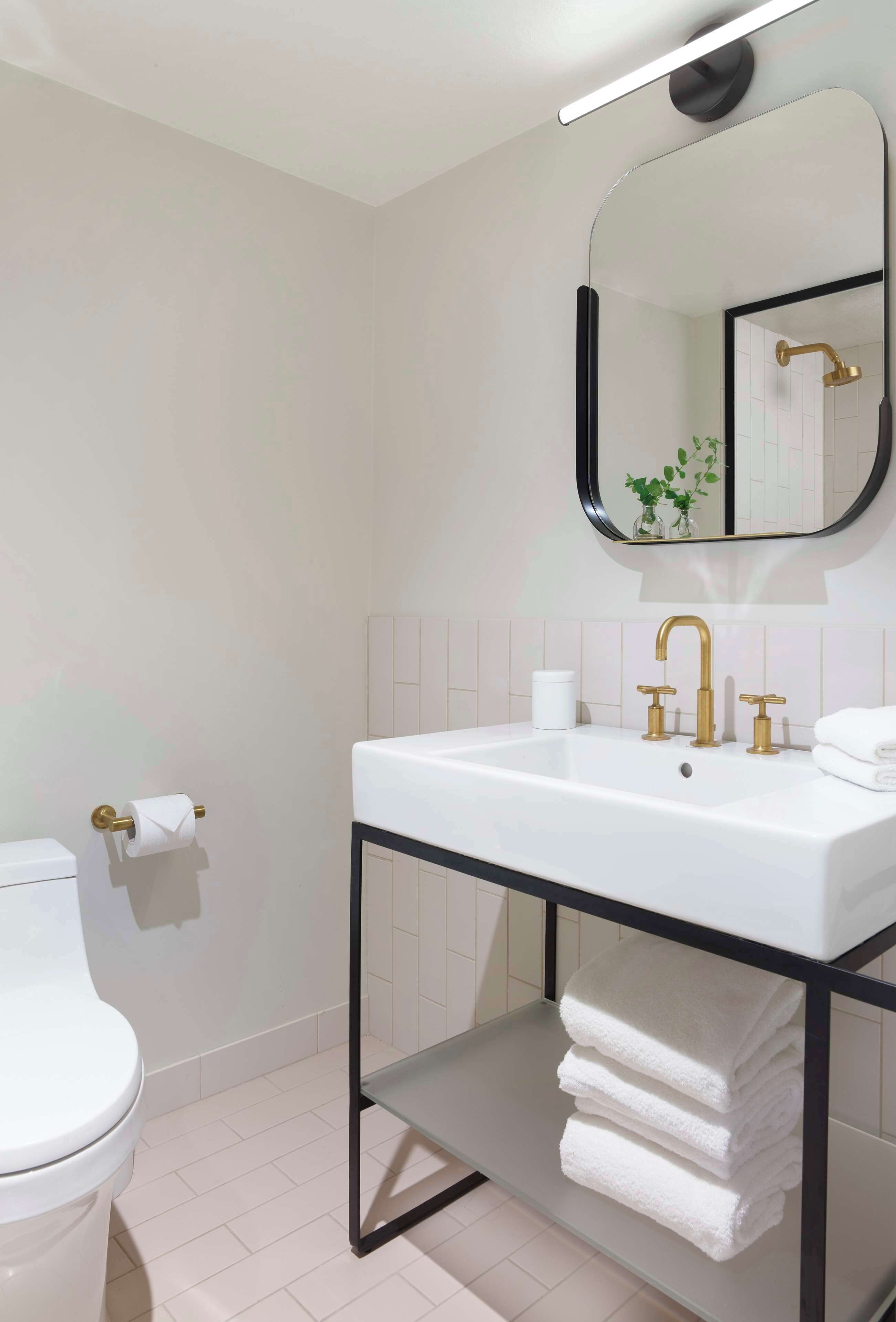 Un baño moderno con un lavamanos blanco, grifería dorada y un espejo con marco negro.