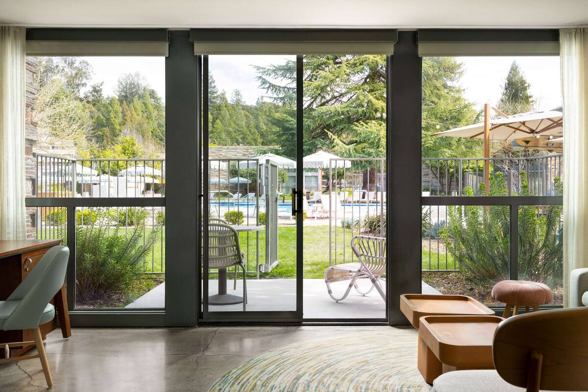Una habitación con un gran ventanal corredera que da a un balcón con vistas a una piscina y zonas verdes.
