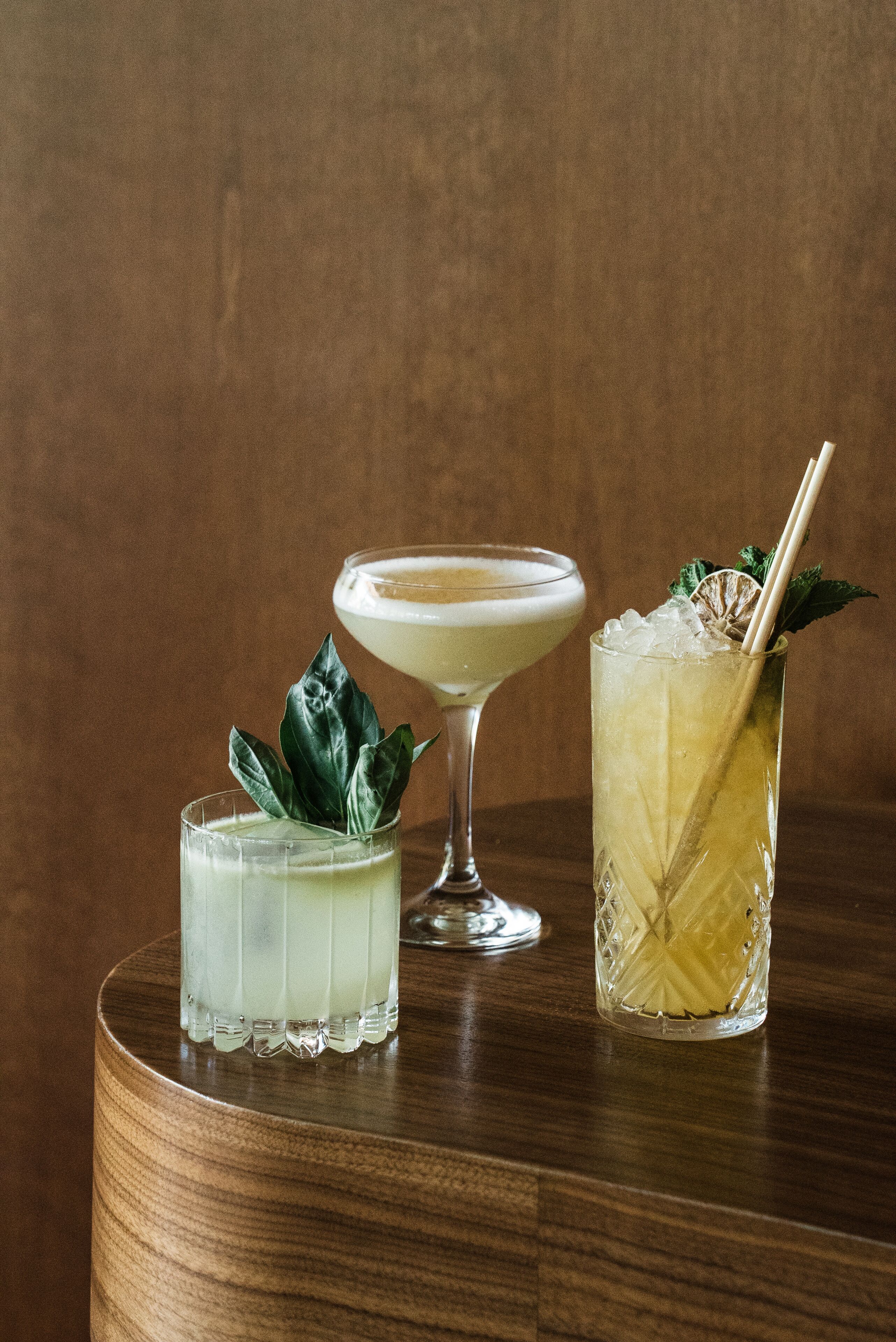 Three cocktails on a wooden table with a brown background.