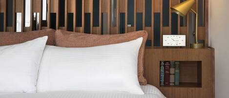A neatly made bed with white linens, a wooden nightstand with a clock and books, and a modern wall with vertical wooden slats.