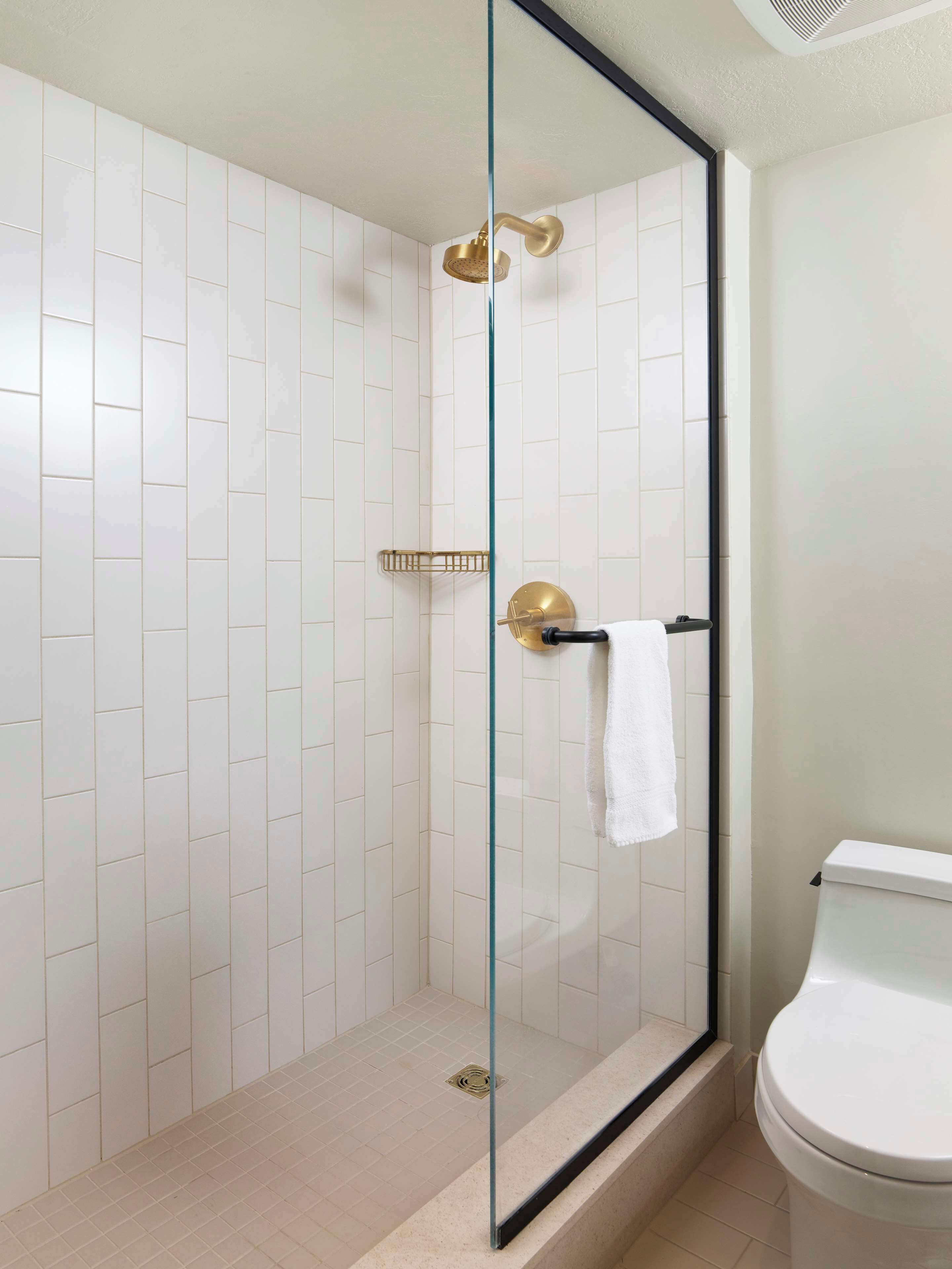 A modern bathroom with a glass-enclosed shower, white tiled walls, and a white toilet.