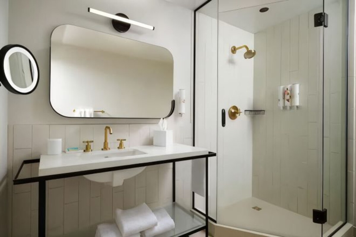 Een moderne badkamer met een douchecabine van glas, een witte wastafel met gouden details en een grote spiegel.