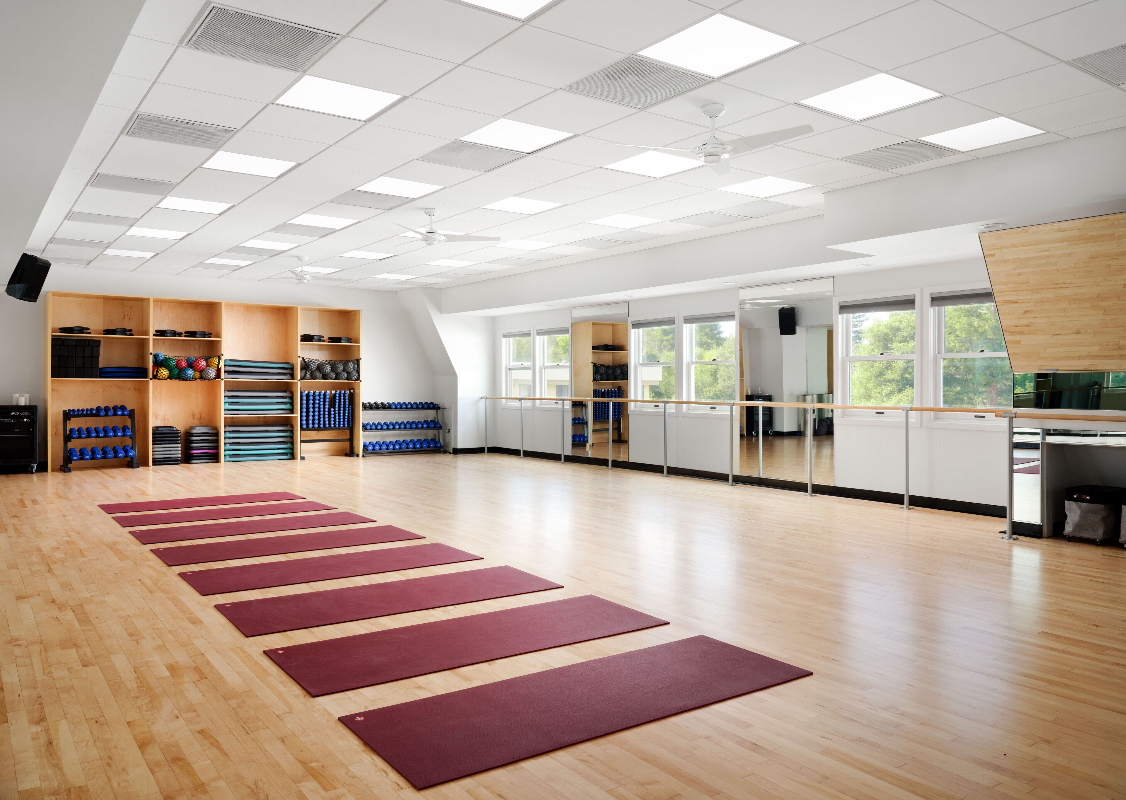A spacious room with wooden floors, a ceiling with square lights, and a ballet barre along one wall.