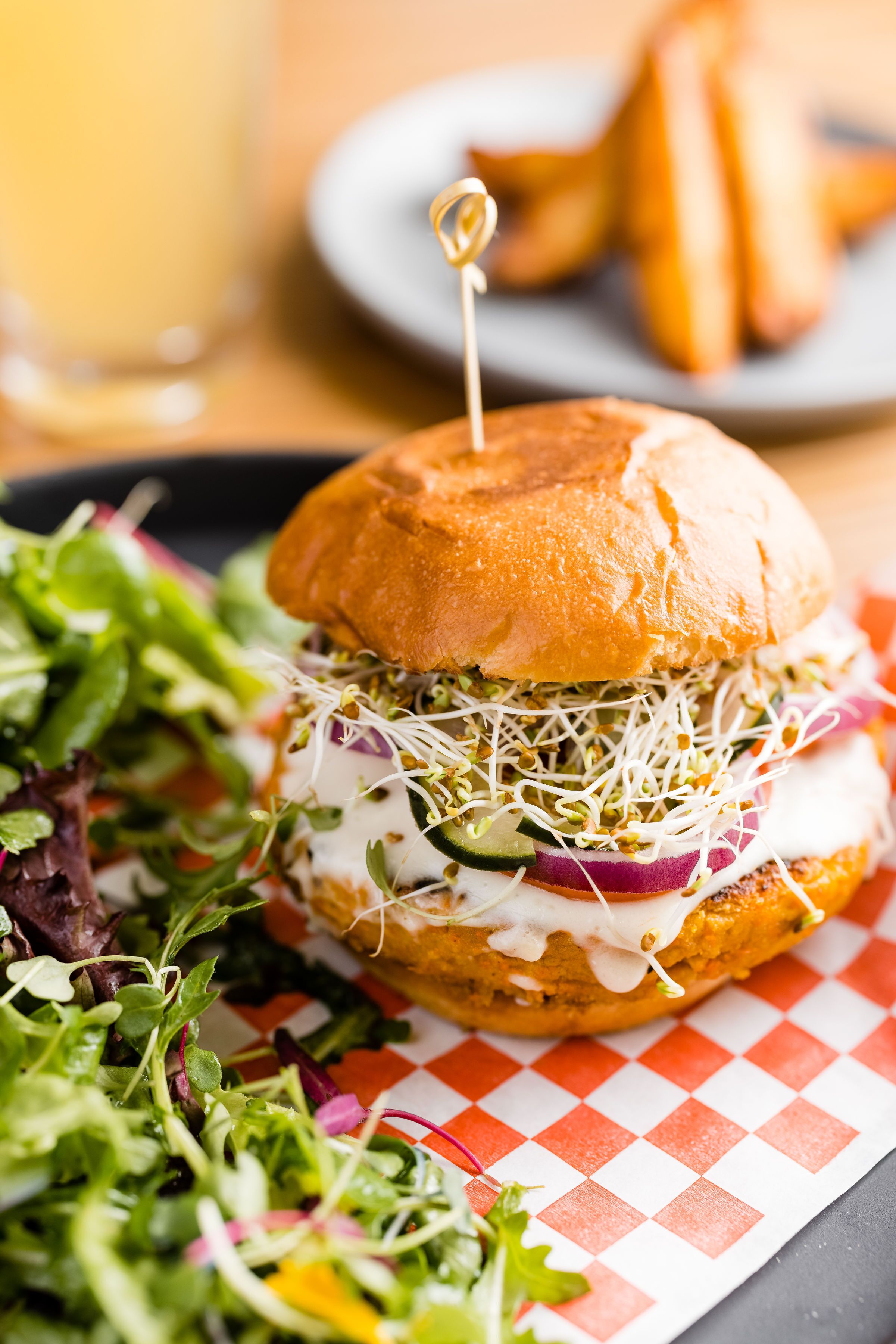 A burger with a toothpick on top, surrounded by a side salad and a drink.