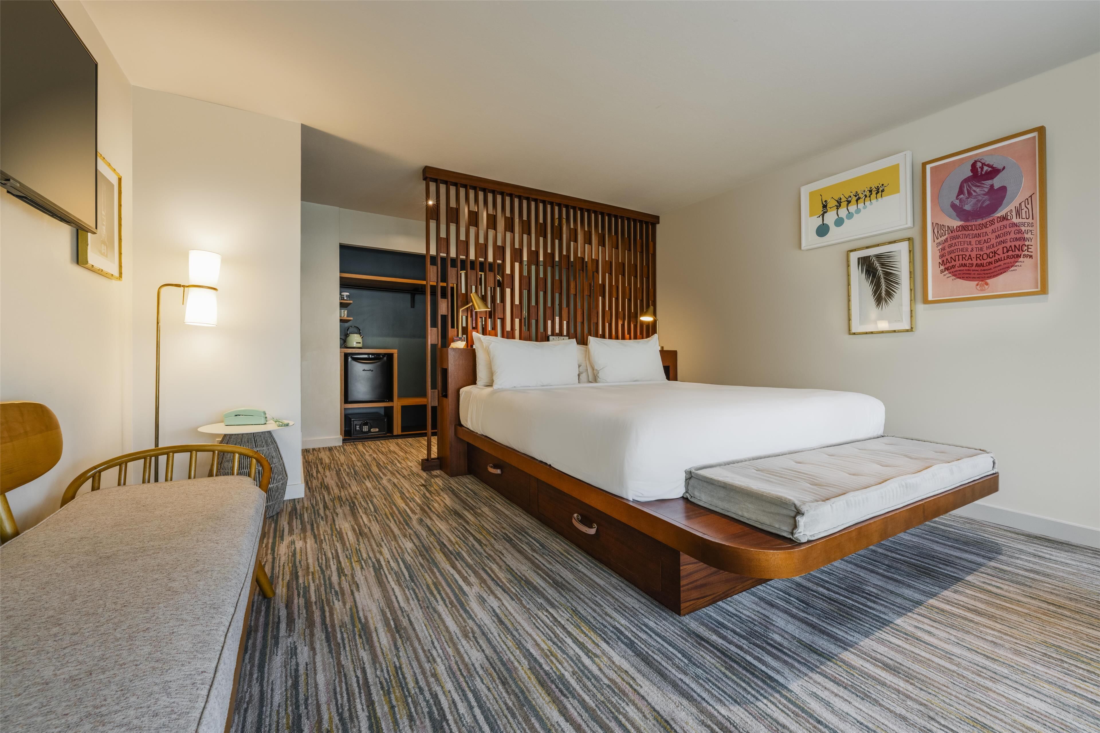A modern hotel room with a large bed, a desk, a chair, and a wardrobe.