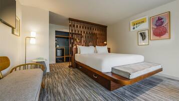 A modern hotel room with a large bed, a desk, a chair, and a wardrobe.