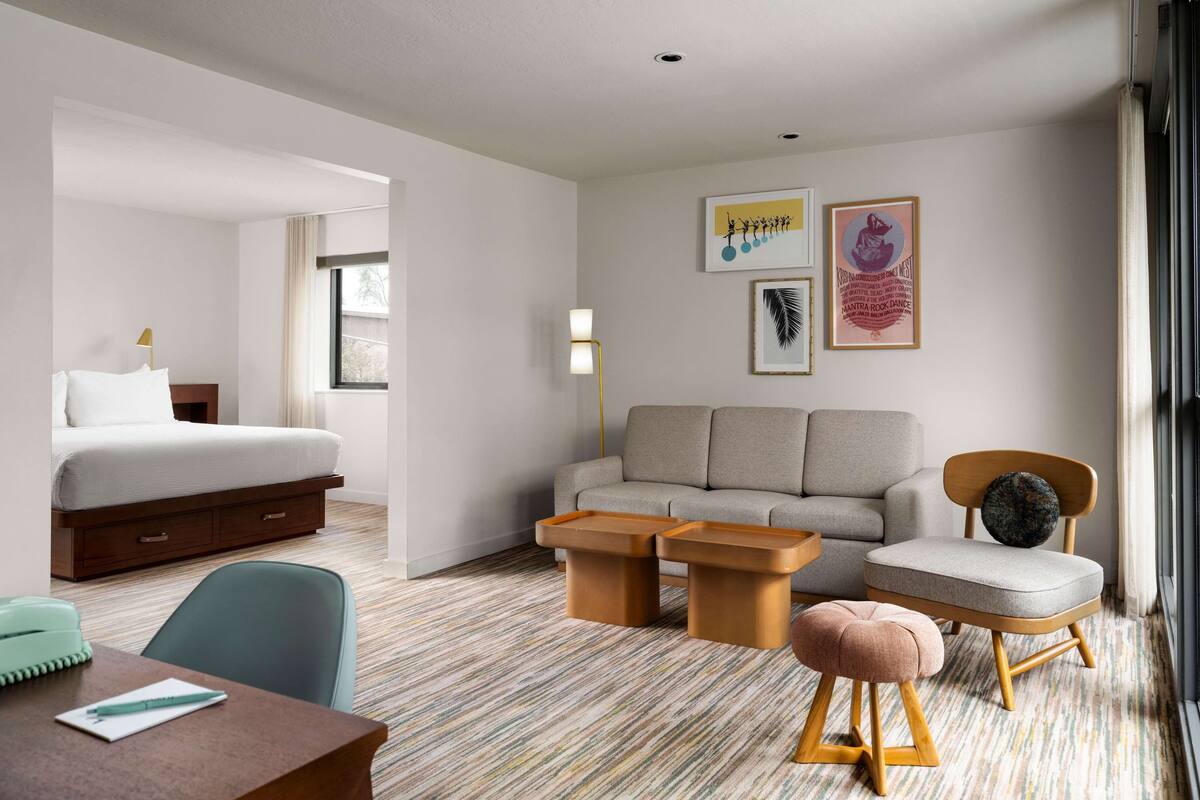 Habitación de hotel con cama, sofá, una mesita de centro, escritorio y una silla. Hay dos cuadros en la pared.